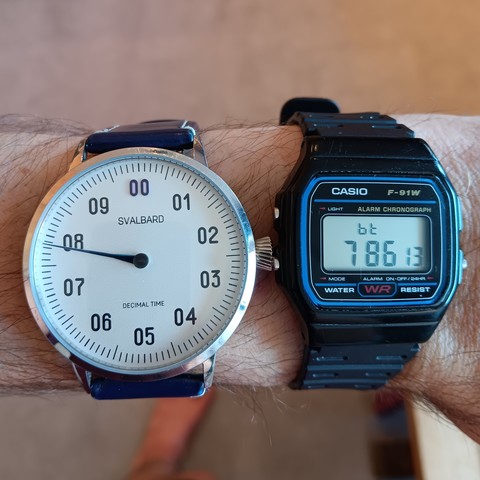 Two watches on the same wrist, one analog and one decimal showing the time as 7.86