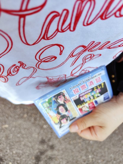 白地に赤い色で英語の文字が入ったTシャツを着て、カラーの投票済証を持った自分の写真。