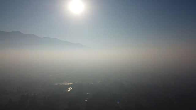Sun rising above the eastern horizon on July 5th. The sky is very hazy with a deep layer of smog over the horizon. The ground is partially visible through the smog.