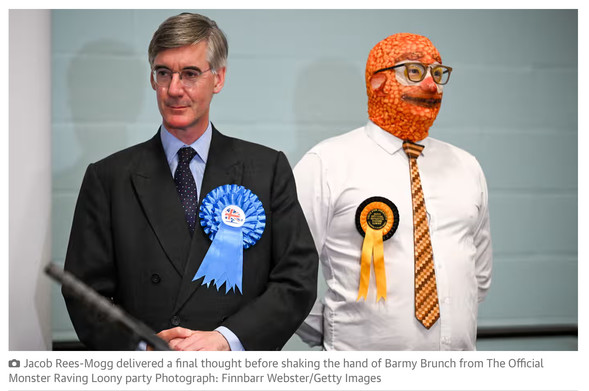 Photo of an appalling Victorian beanpole wearing a rosette big enough for a horse, standing beside a man whose shirt and tie are complemented perfectly by a ski mask patterned to make his head look like a baked-bean covered fried breakfast. Caption: Jacob Rees-Mogg delivered a final thought before shaking the hand of Barmy Brunch from The Official Monster Raving Loony party Photograph: Finnbarr Webster/Getty Images