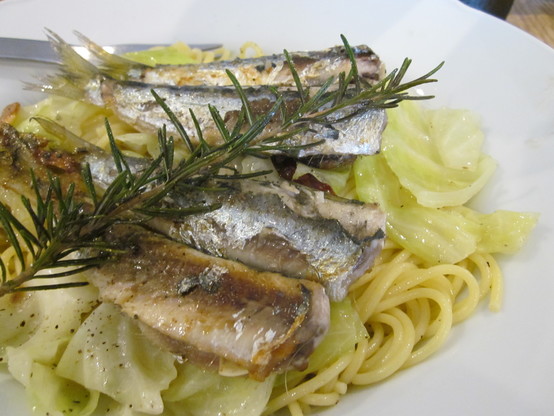 Close up on a plate of spaghetti peperoncino with a topping of pan fried fresh sardines with a sprig of rosemary