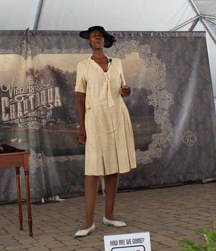 A Black woman, in 1920s dress and portraying Zora Neale Hurston, stands onstage in a dignified pose. 