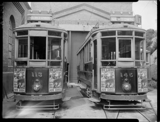 Black-and-white photo:  Newtown trams no 113 and 145, Wellington, with advertisements for The Ten Commandments showing at the De Luxe theatre. 1924. Photograph taken by Crown Studios of Wellington. Citation: Crown Studios Ltd: Negatives and prints. Ref: 1/1-032600-F. Alexander Turnbull Library, Wellington, New Zealand. https://natlib.govt.nz/records/23136719