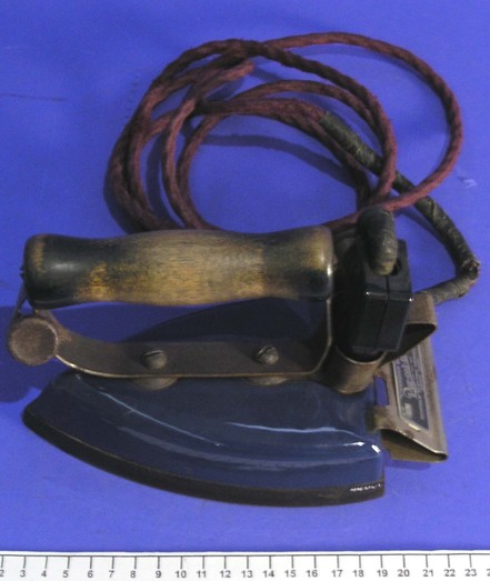 Colour photo: Iron, electric. ca. 1925. Description: Electric iron, ‘Canadian Beauty’, made by Renfrew Electric and Refrigeration Company, Ontario, Canada. It has a dark blue base and wooden handle. The rusty-brown power cord is plugged in towards the back, between the handle and the metal ‘foot’. Citation: Auckland War Memorial Museum Tāmaki Paenga Hira, CC BY, ID No. NN214. https://www.aucklandmuseum.com/collection/object/am_humanhistory-object-650822