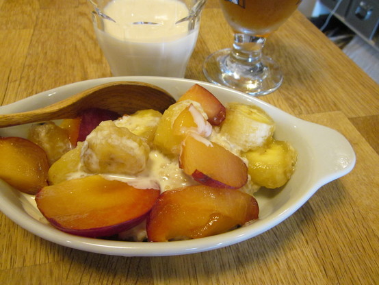 A close up of a dish of porridge with plum and banana chunks and a splash of soy milk.  A glass of cold soy milk and of iced tea in the background.