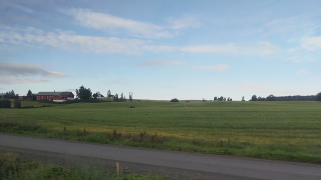 Commute photo along Stange, Norway. Green fields with a red barn house on the left side.