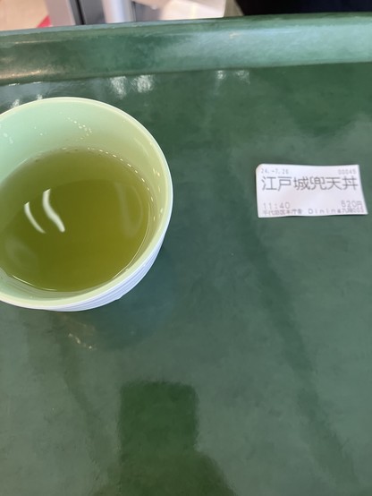 A cup of green tea on a green tray next to a printed receipt in Japanese.