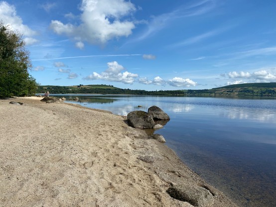 Blessington lake showing beach in foreground and hills in the distance on the other side. Puffy clouds on a warm day. 