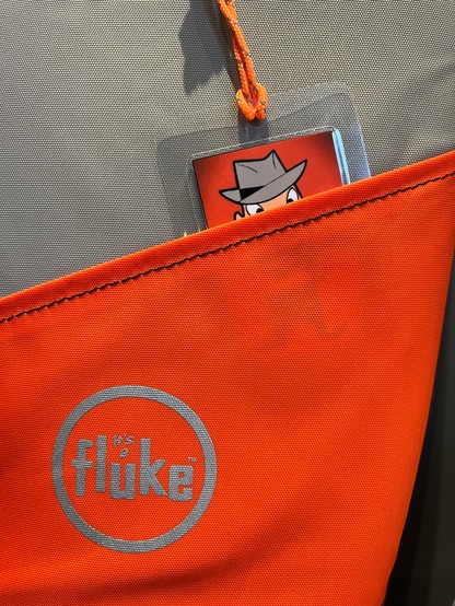 Photo of the lower part of a padded instrument bag in grey and orange material with a circular silver logo containing the text 