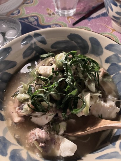 A bowl of soup with tofu, tinned mackerel, chopped myoga and shiso herbs, with a spoon in the broth. 