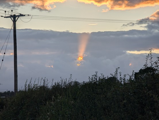 Clouds with a gap with sun shining through that vaguely look like a smiling mouth, hands, and eyes with a sunbeam shining out of them.