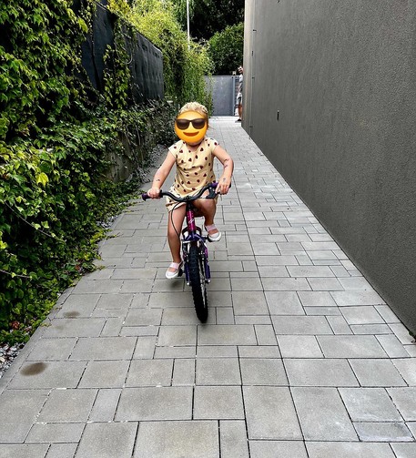 A little girl in a skirt riding a bike in an aisle. Her face is covered by the sunglasses emoji.