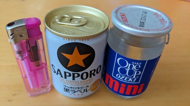 高さ８センチ程の大きさのビール缶とガラス瓶入りの日本酒。日本の報道写真では古来から身近によくある物品を大きさ比較の為に一緒に並べて撮影したものです。それがこの左に置いたライター！近年、禁煙が定着して、持っている人を探すのが難しくなりました。