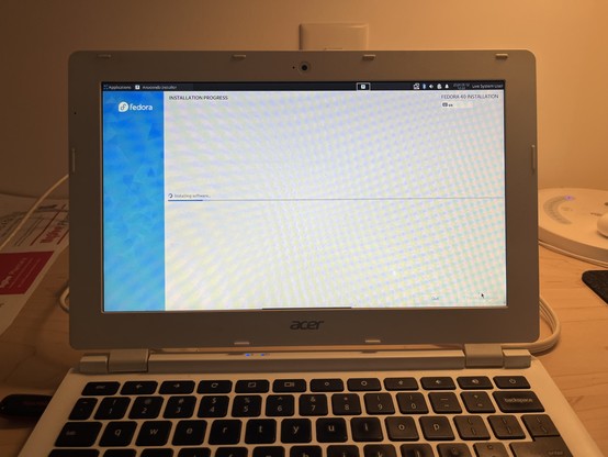 Photo of a laptop on a desk. The screen is mostly blank, with only an installation screen showing fedora being installed. 