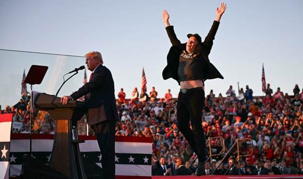 Donald Trump blathering incontinently at a fascist rally while Elon Musk jumps up and down like Zebedee tripping balls.