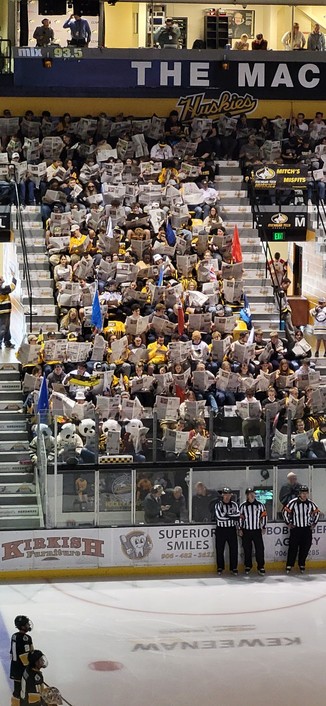 The MTU hockey student section.
Every single person has their head buried in open copies of the school newspaper. This is done while the opposing team is being introduced.
Three referees wait at the edge of the ice.