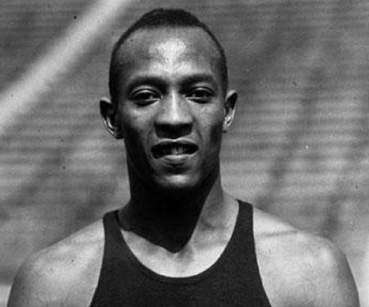 Monochrome photograph of Jesse Owens looking directly at the camera, wearing a running vest